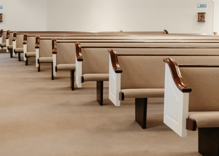 Rows of reupholstered beige church pews with dark wood ends
